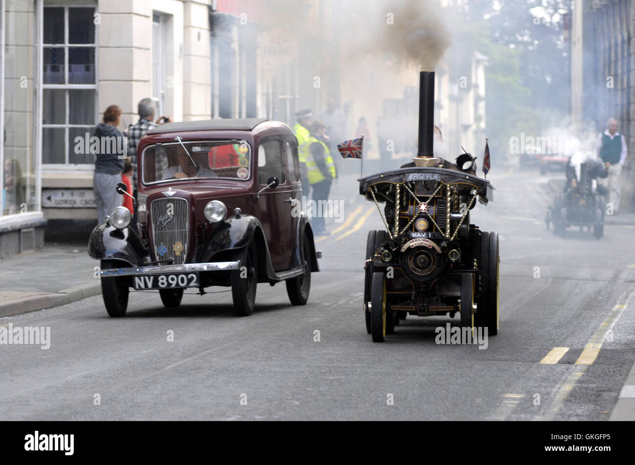 Kington, Herefordshire, UK. 21st August 2016.  A miniature steam engine is over taken by an old Austin Seven as it makes its way up Kington High Street. Credit:  Andrew Compton/Alamy Live News Stock Photo