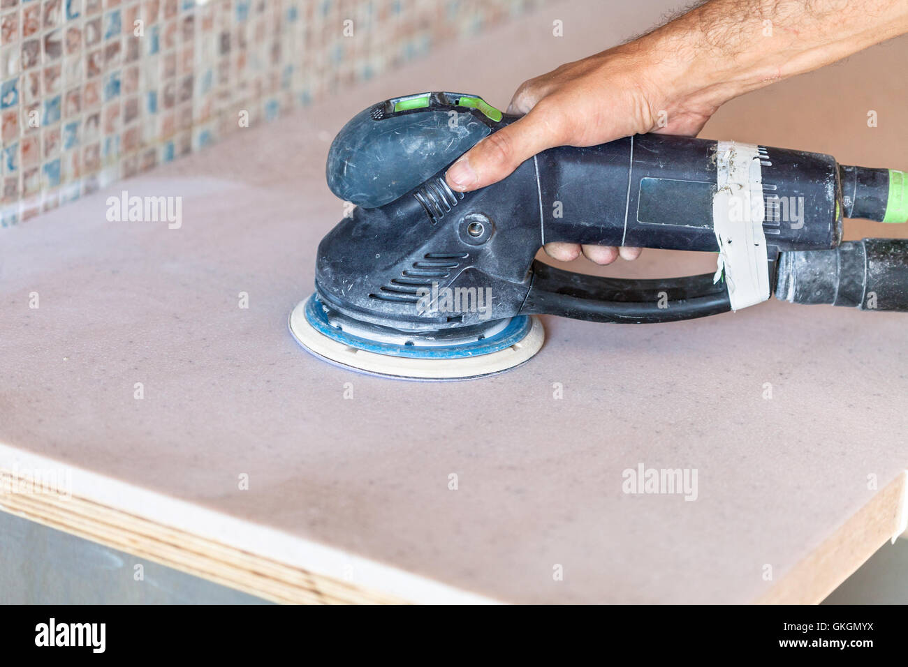 installing new tabletop on kitchen - worker sanding countertop from artificial stone by random orbital sander Stock Photo