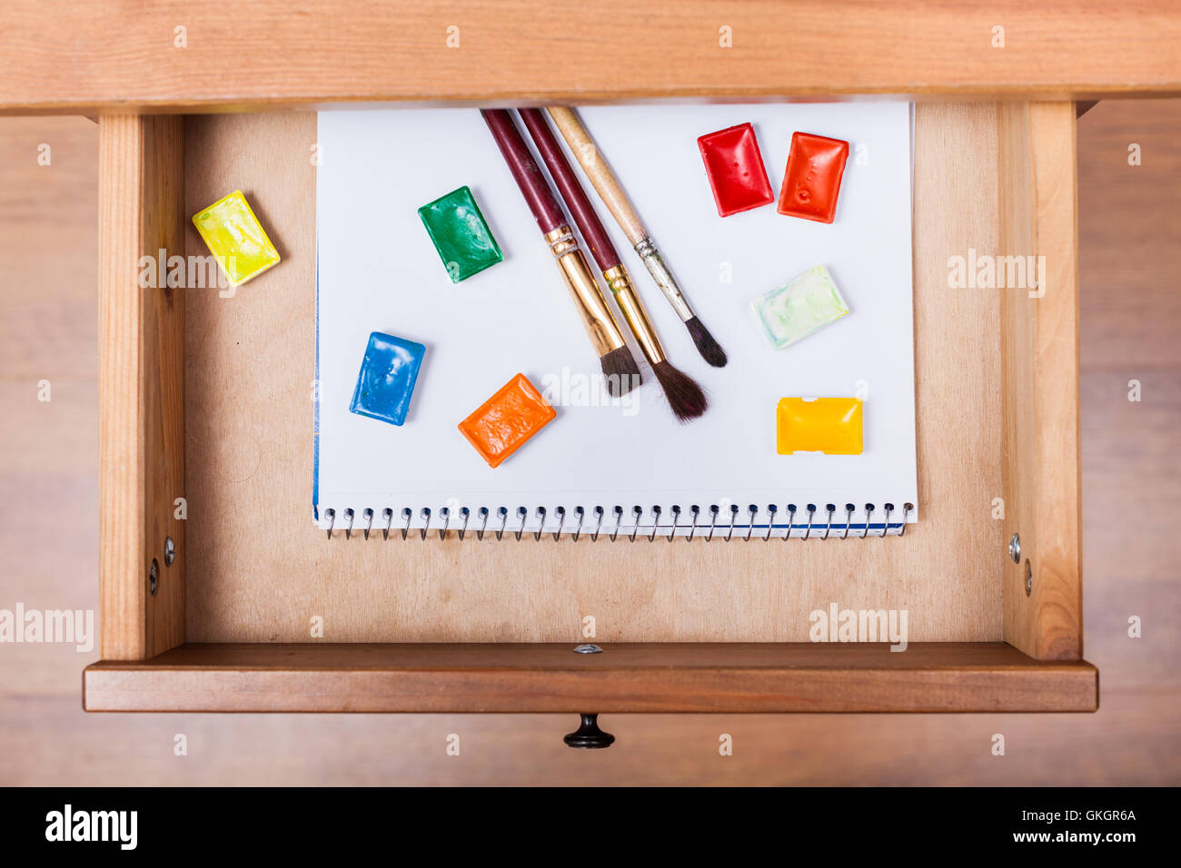 above view of paint brushes and water paints on album in open drawer of nightstand Stock Photo