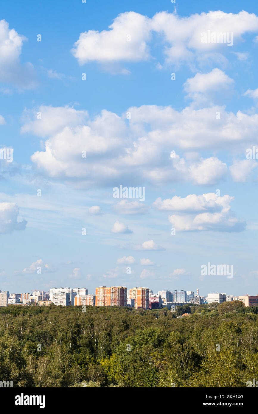 white clouds in blue sky over city and green woods in sunny summer day ...
