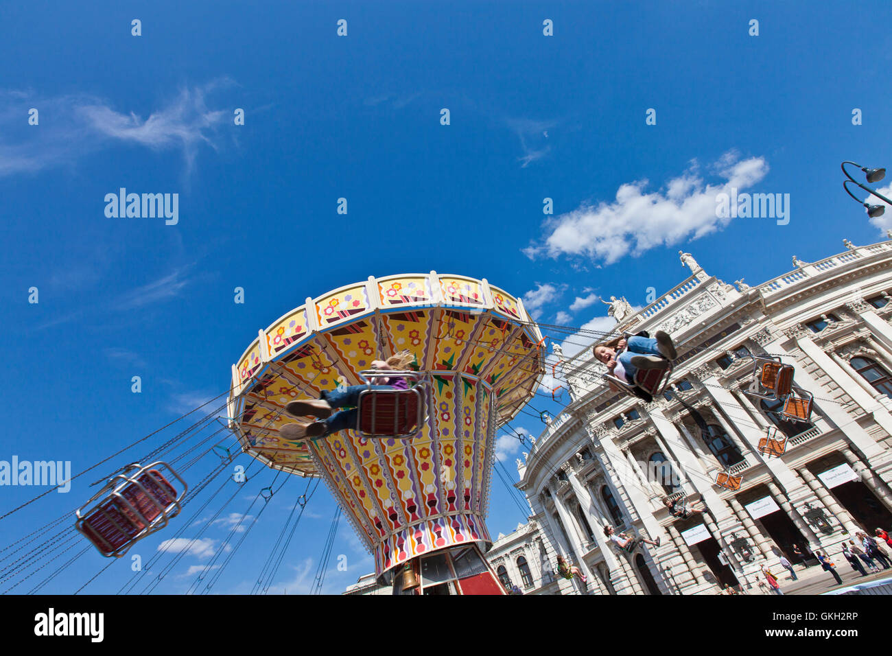 The historic Imperial Court Theatre at the famous Viennese Ringstrasse with some people enjoy a ride ona vintage carousel Stock Photo