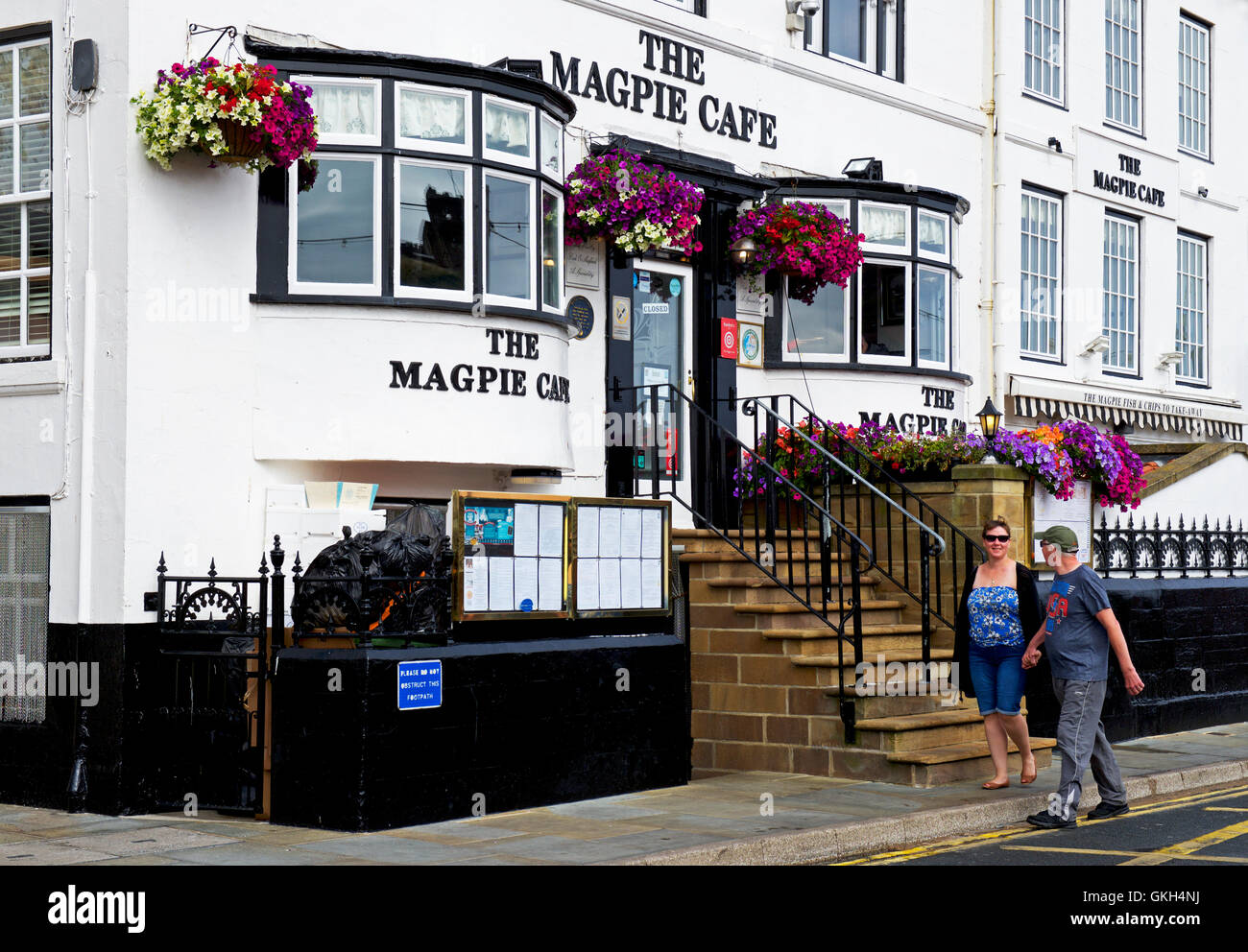 Young couple walking past the Magpie Café, Whitby, North Yorkshire, England UK Stock Photo