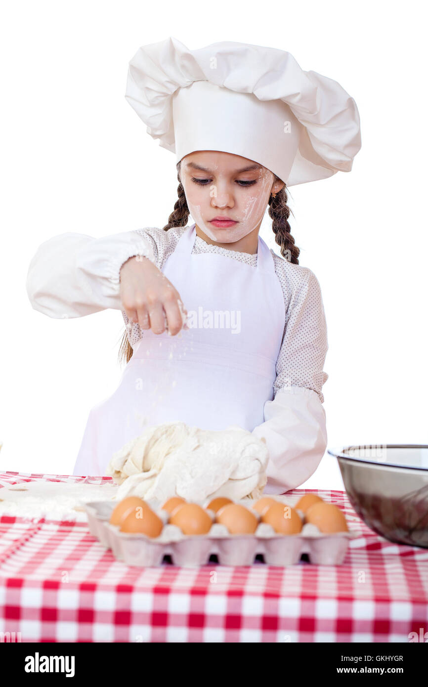 Portrait of a little girl in a white apron and chefs hat knead the dough in the kitchen, isolated on a white background Stock Photo