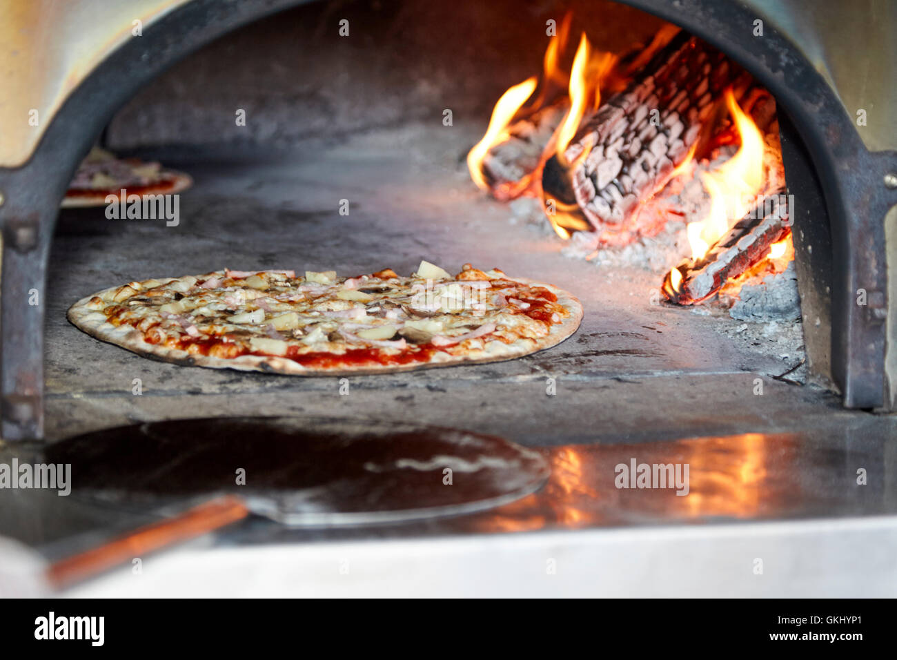 ham and pineapple thin crust pizza cooking in a wood fired pizza oven
