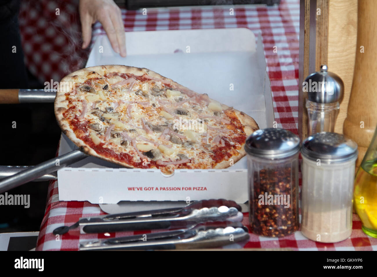 ham and pineapple thin crust pizza being placed in a takeaway box Stock Photo