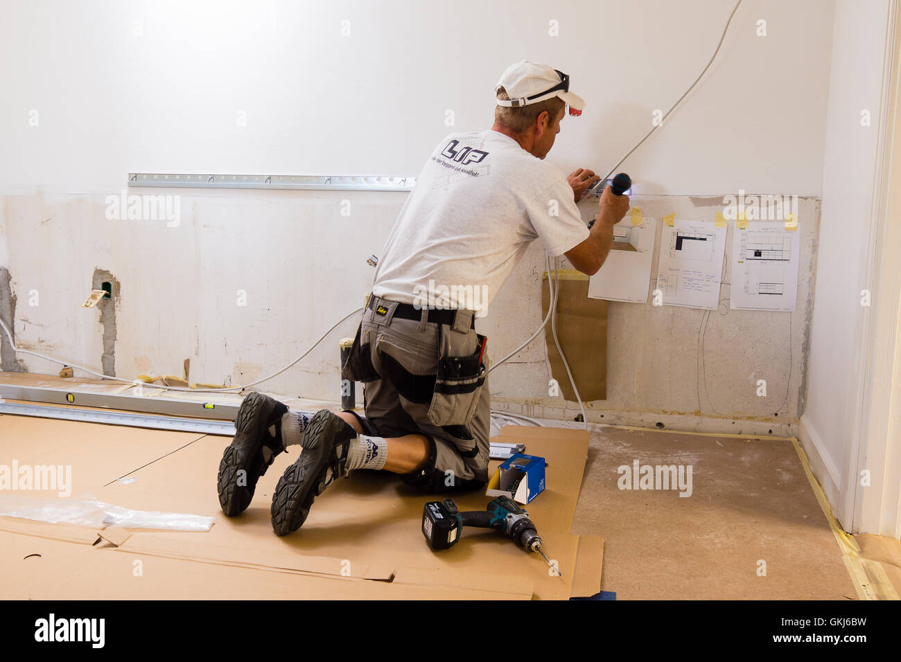 Carpenter mounting an IKEA kitchen with screwdriver and has blueprints on the wall. Stock Photo