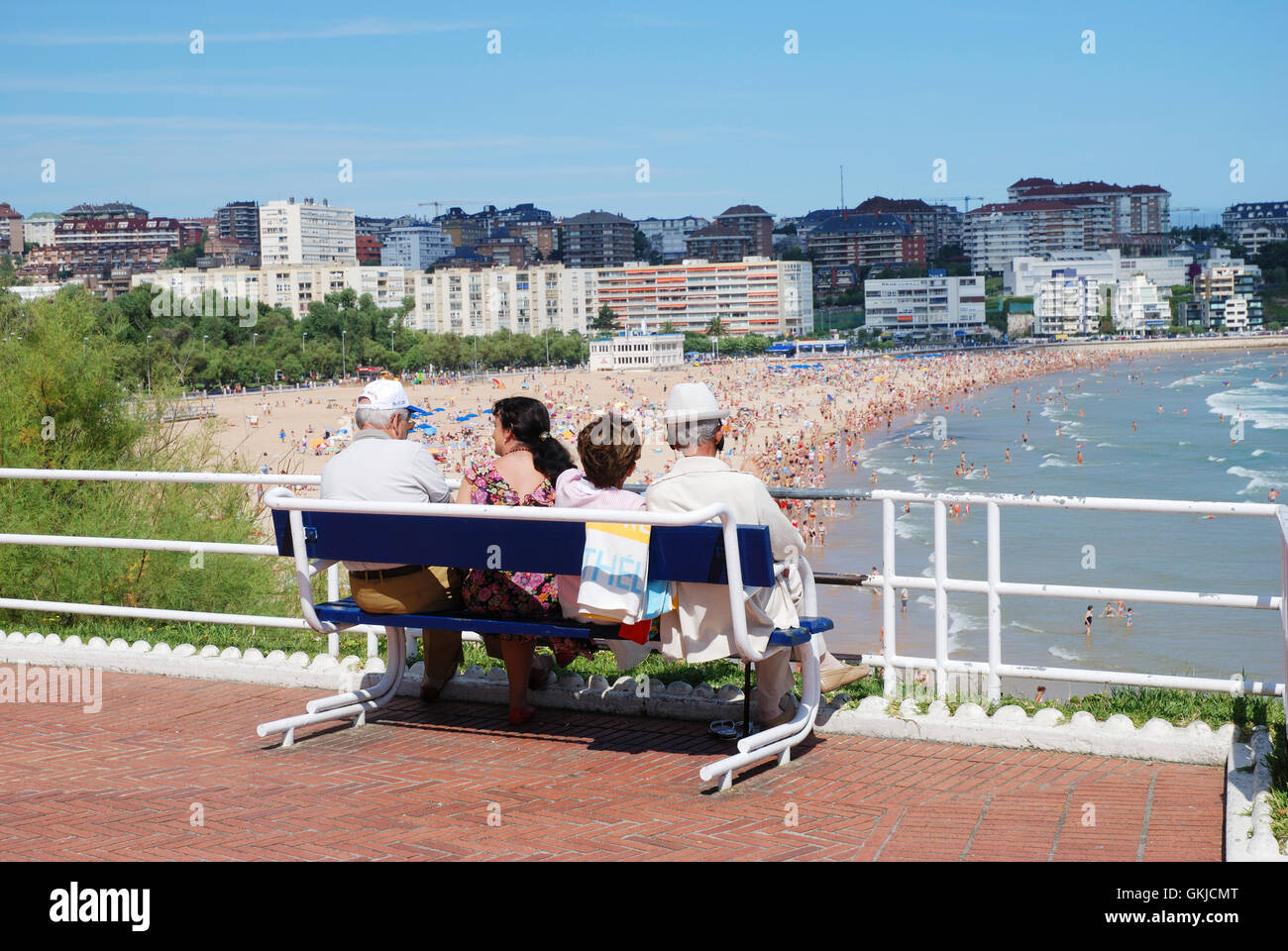 Four people sitting on a bench looking at the beach. Piquio gardens, Santander, Spain. Stock Photo