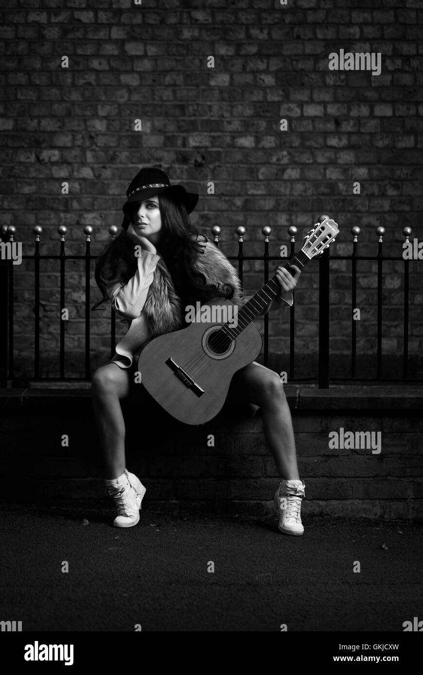 Country music star performer female, sitting on brick wall with brick backdrop Stock Photo