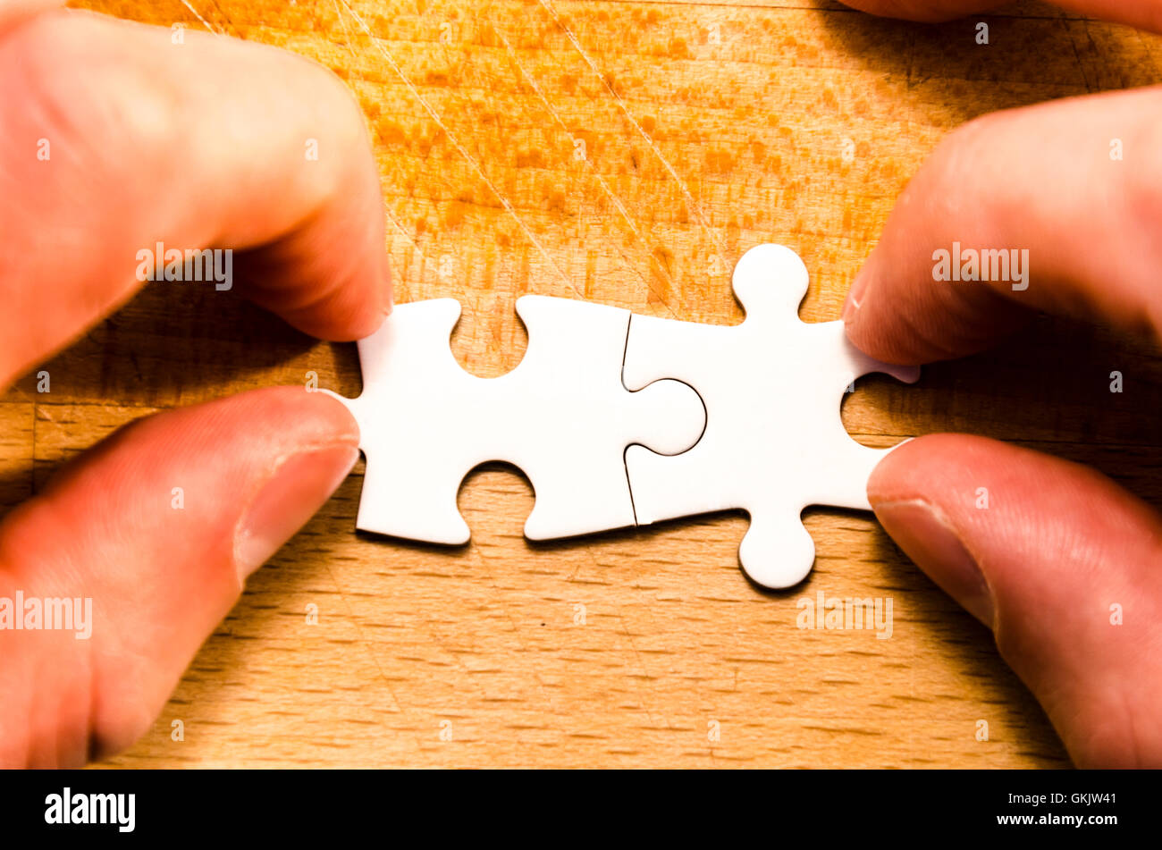 first two pieces of white jigsaw/puzzle over a wooden table background, symbol of problem solving Stock Photo