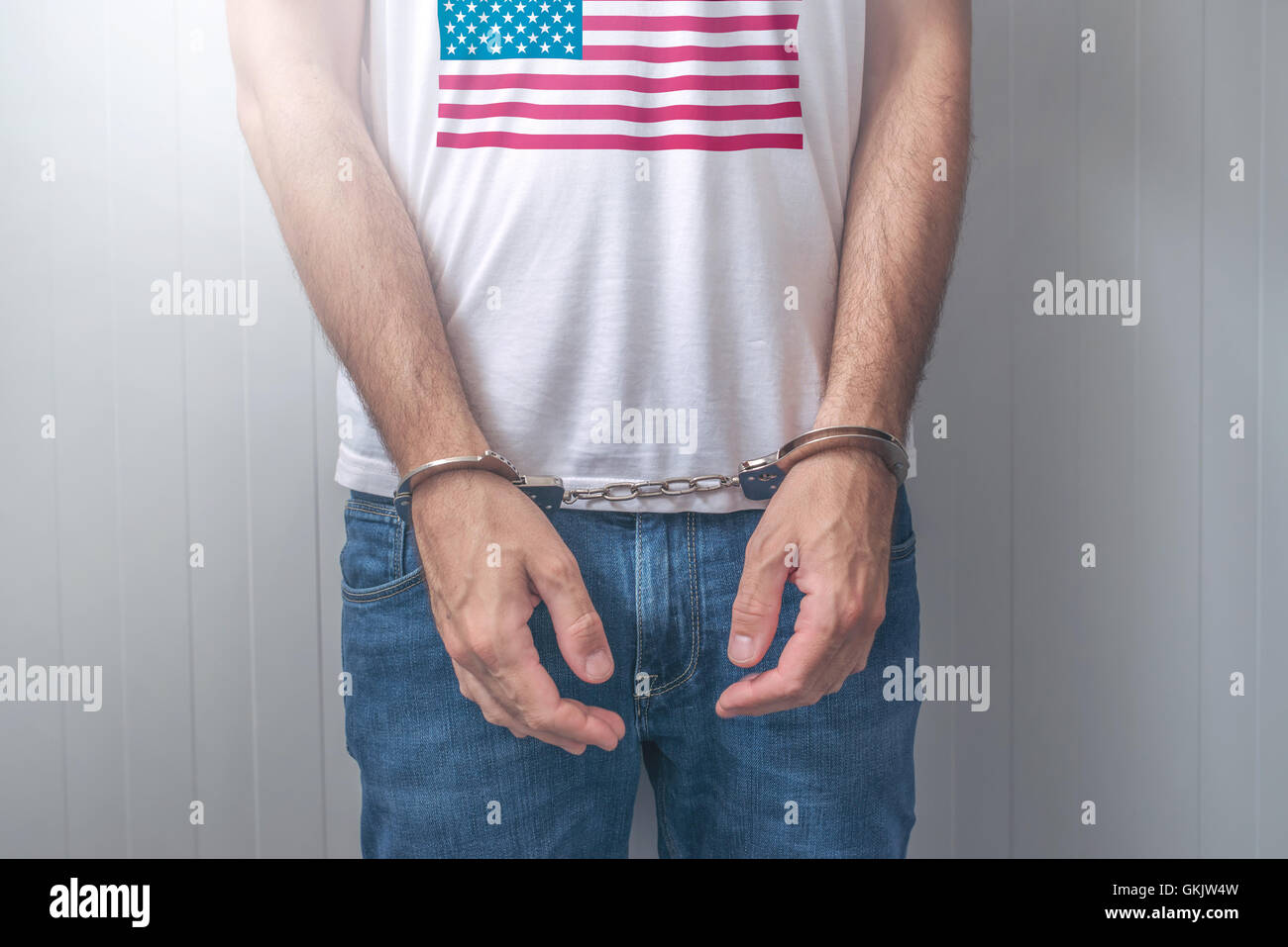 Arrested man with cuffed hands wearing shirt with USA flag. Unrecognizable male person in jeans with handcuffs held in police st Stock Photo