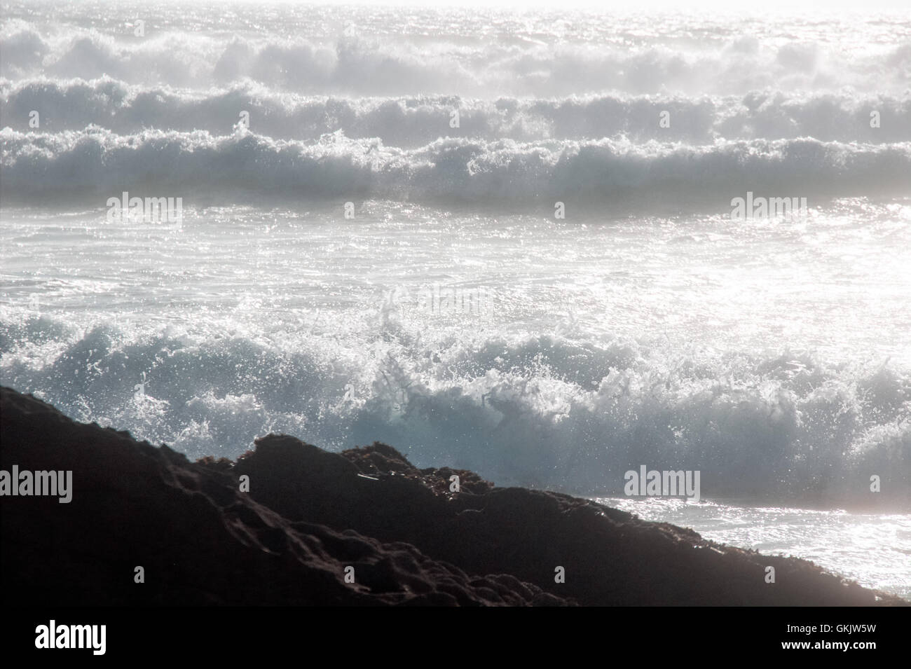 Four ocean waves rolling towards the rock on the shore, foaming and breaking Stock Photo