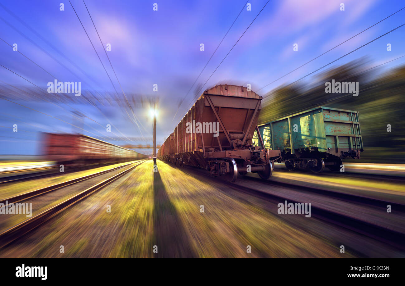 Railway station with cargo wagons in motion at night. Railroad with motion blur effect. Heavy industry Stock Photo