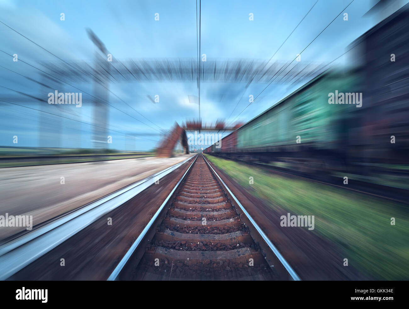 Railway station with cargo wagons in motion at sunset. Railroad with motion blur effect. Railway platform at dusk. Heavy industr Stock Photo