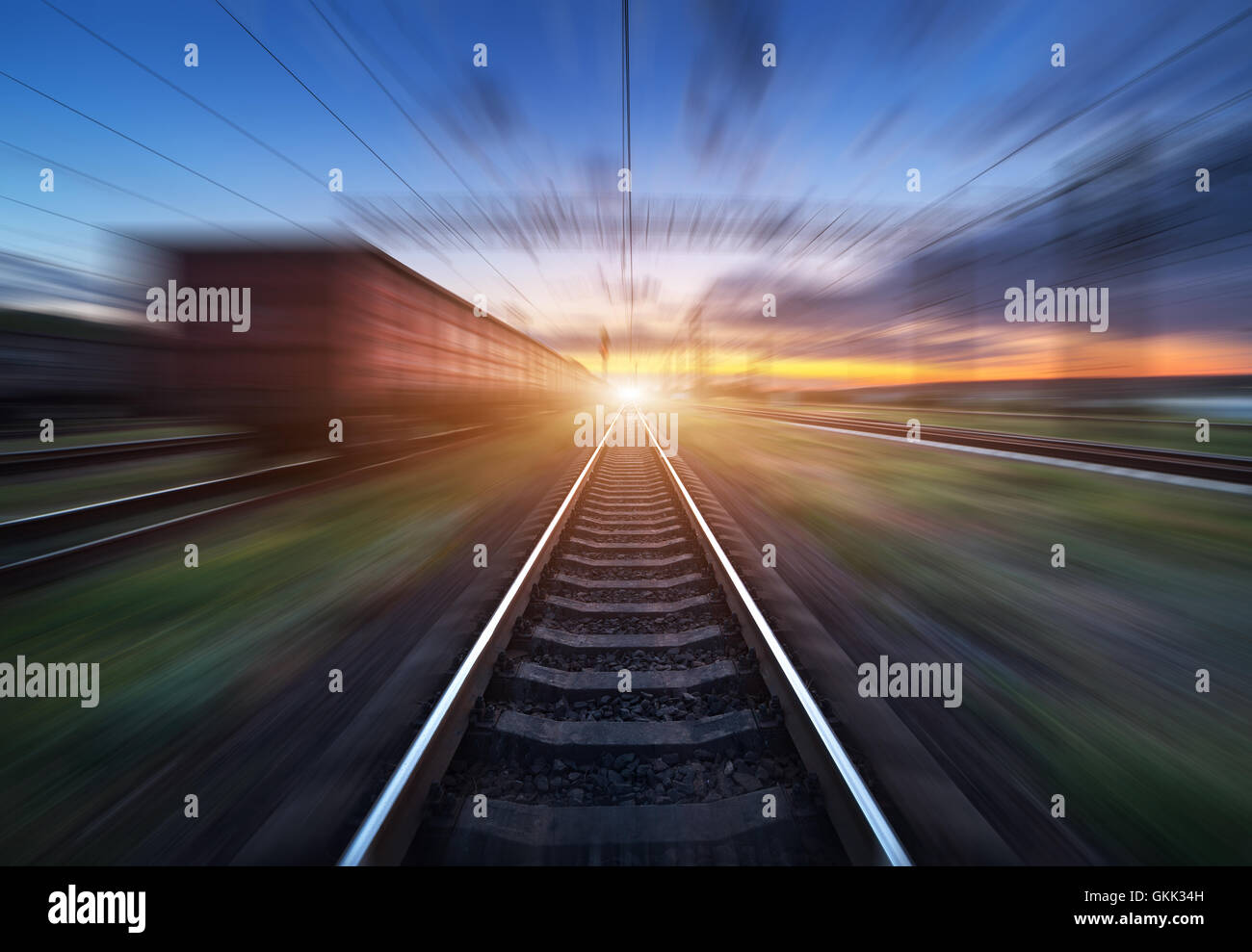 Railway station with cargo wagons and train light in motion at sunset. Railroad with motion blur effect. Railway platform. Heavy Stock Photo