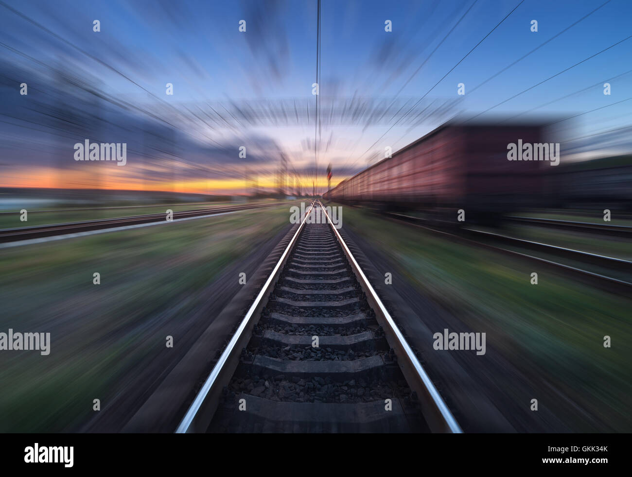 Railway station with cargo wagons in motion at sunset. Railroad with motion blur effect. Railway platform at dusk. Heavy industr Stock Photo