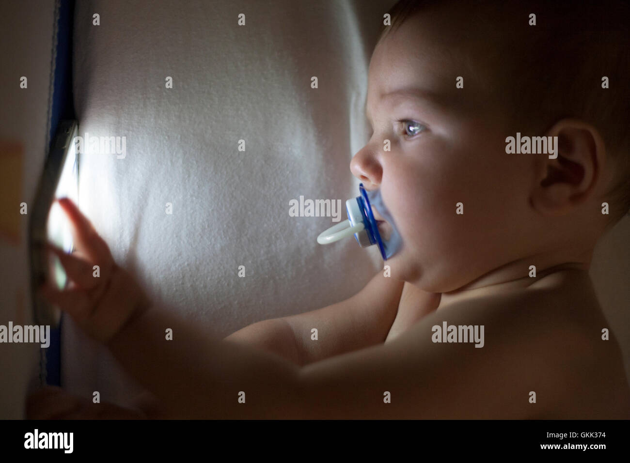 12 month old baby using mobile phone on the crib at night Stock Photo