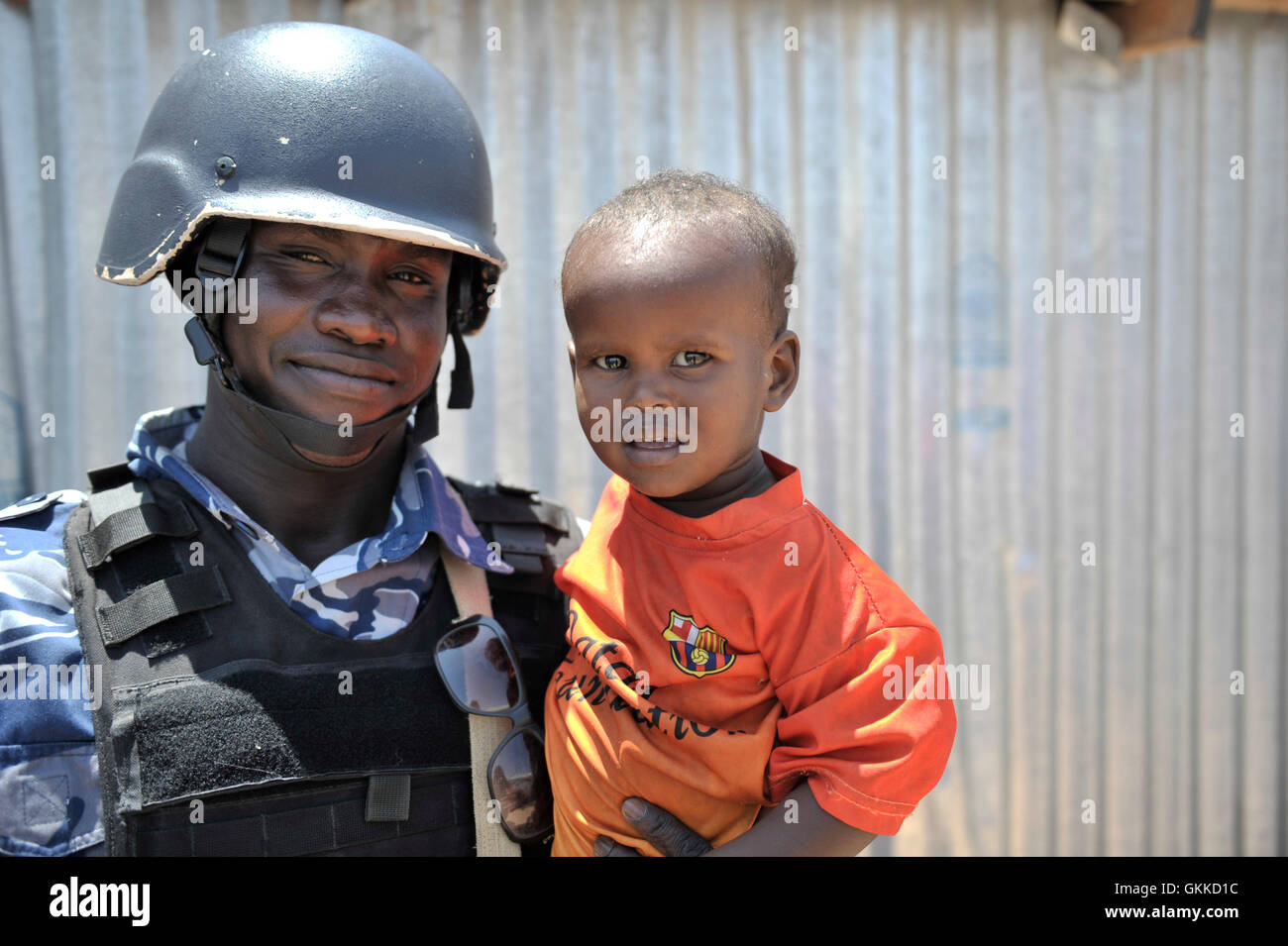 An AMISOM police officer holds a young Somali boy at an IDP camp, Siliga Amerikanka, on 24th February 2014 after a foodstuff donation. The donation comprised of 10 bags of rice, 3 bags of maize, 3 bags of cow peas, 3 bags of sugar, salt and 20 gallons of oil. AU UN IST PHOTO / DAVID MUTUA Stock Photo