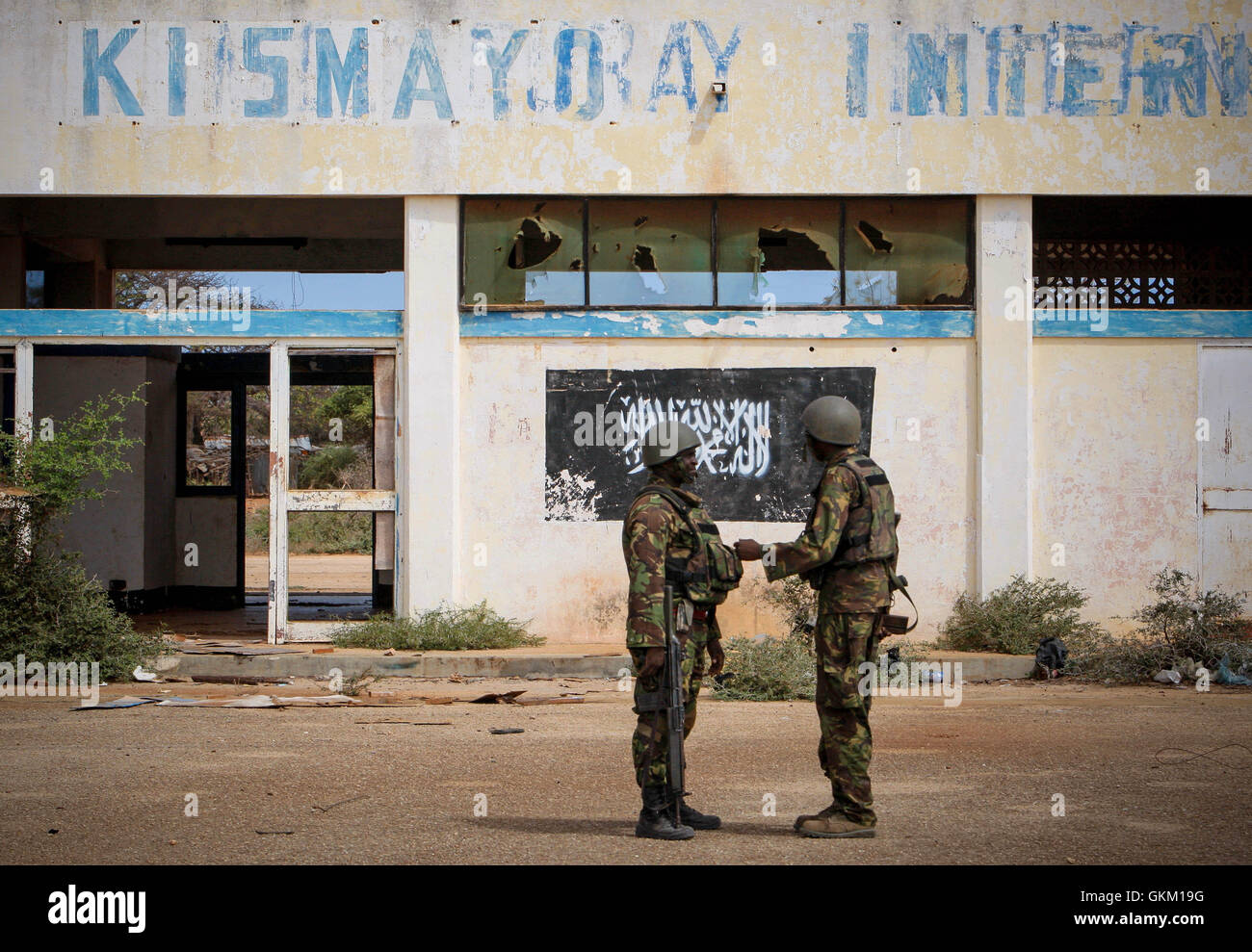 SOMALIA, Kismayo: In a handout photograph released by the African Union-United Nations Information Support Team 02 October, soldiers of the Kenyan Contingent serving with the African Union Mission in Somalia (AMISOM) stand in front of the black flag of the Al Qaeda-affiliated extremist group Al Shabaab painted on the wall of Kismayo Airport. Kenyan AMISOM troops moved into and through Kismayo, the hitherto last major urban stronghold of tAl Shabaab, on their way to the airport without a shot being fired following a two-month operation to liberate towns and villages across southern Somalia and  Stock Photo