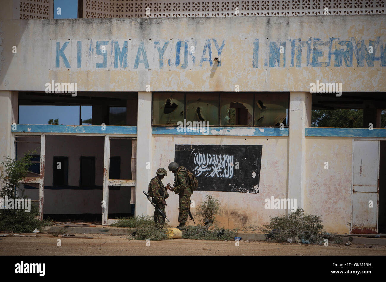 SOMALIA, Kismayo: In a handout photograph released by the African Union-United Nations Information Support Team 02 October, soldiers of the Kenyan Contingent serving with the African Union Mission in Somalia (AMISOM) stand in front of the black flag of the Al Qaeda-affiliated extremist group Al Shabaab painted on the wall of Kismayo Airport. Kenyan AMISOM troops moved into and through Kismayo, the hitherto last major urban stronghold of tAl Shabaab, on their way to the airport without a shot being fired following a two-month operation to liberate towns and villages across southern Somalia and  Stock Photo