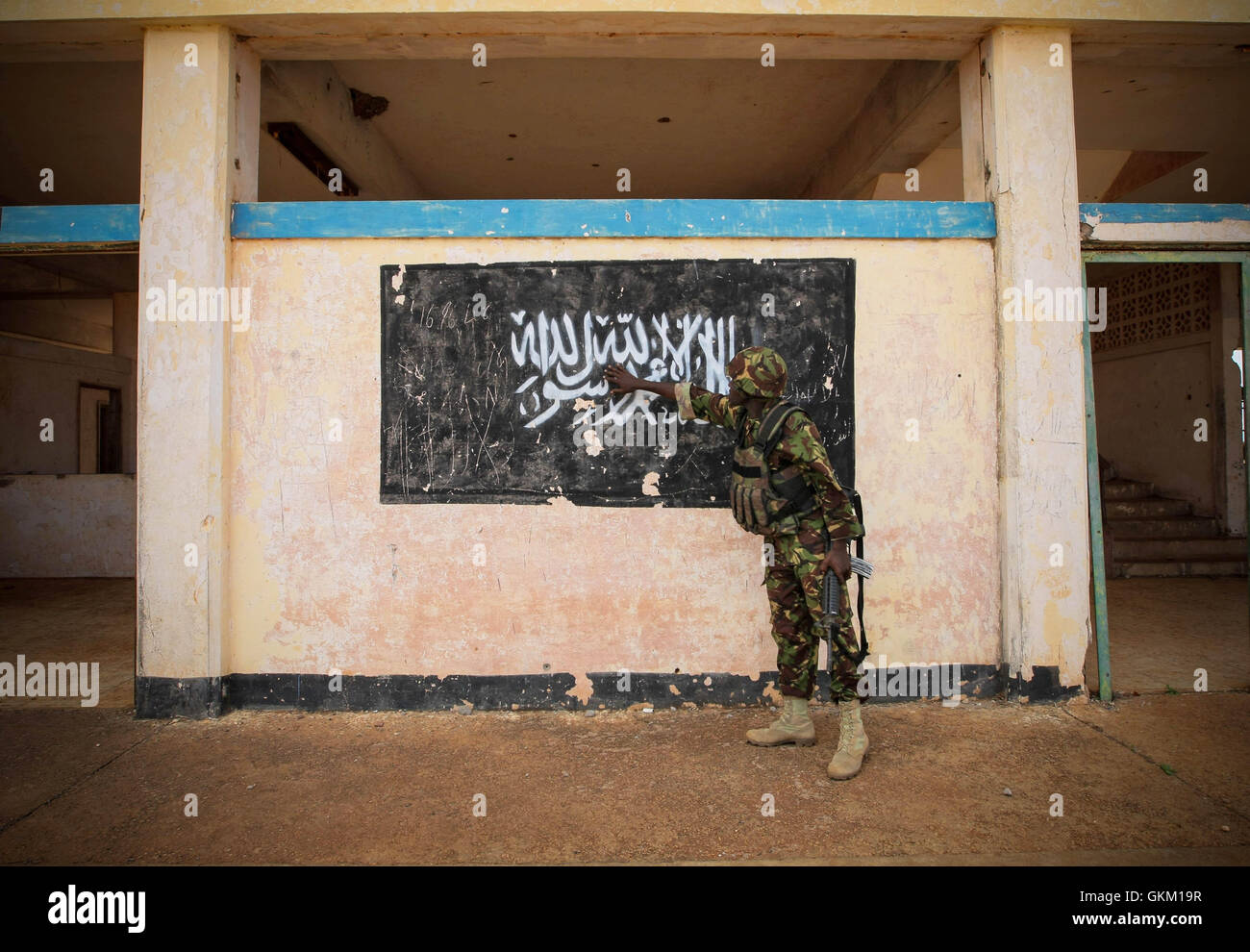SOMALIA, Kismayo: In a handout photograph released by the African Union-United Nations Information Support Team 02 October, a soldier of the Kenyan Contingent serving with the African Union Mission in Somalia (AMISOM) gestures towards the black flag of the Al Qaeda-affiliated extremist group Al Shabaab painted on the wall of Kismayo Airport. Kenyan AMISOM troops moved into and through Kismayo, the hitherto last major urban stronghold of tAl Shabaab, on their way to the airport without a shot being fired following a two-month operation to liberate towns and villages across southern Somalia and  Stock Photo