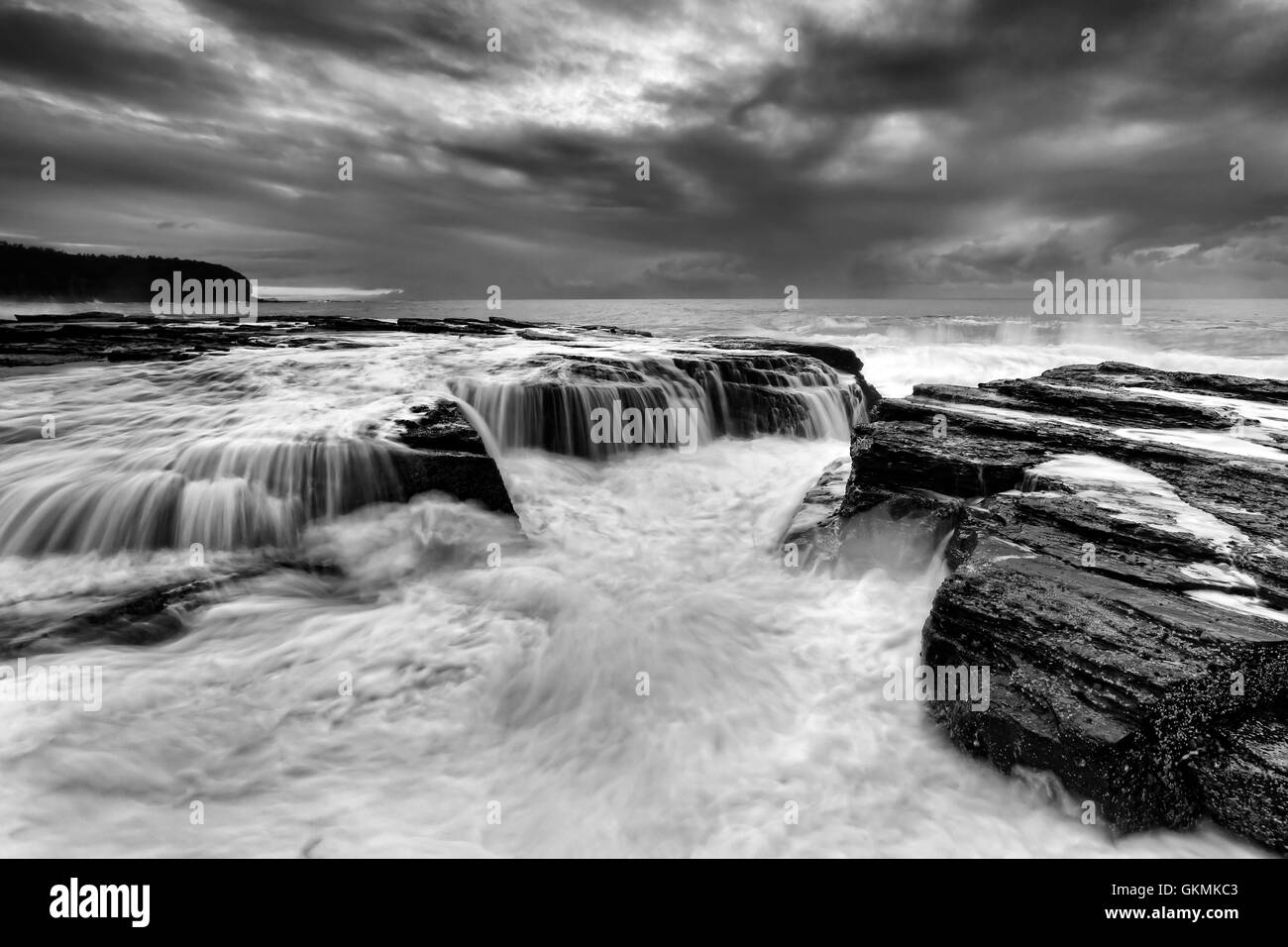dramatic rugged coastal seascape near Collaroy beach in Sydney at sunrise. Black-white image of surfing waves undermining rocks Stock Photo