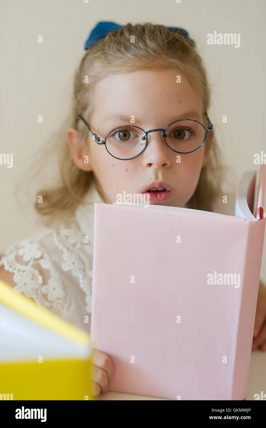 Lovely small student reads. Schoolgirl bespectacled holds the textbook. She has serious look. Stock Photo