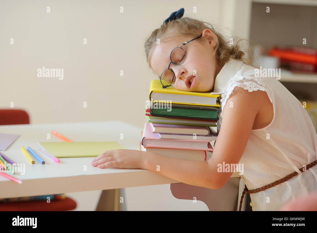 Little schoolgirl fall asleep on a pile of books. Tired girl with glasses rested her head on the book. To kids difficultly long Stock Photo