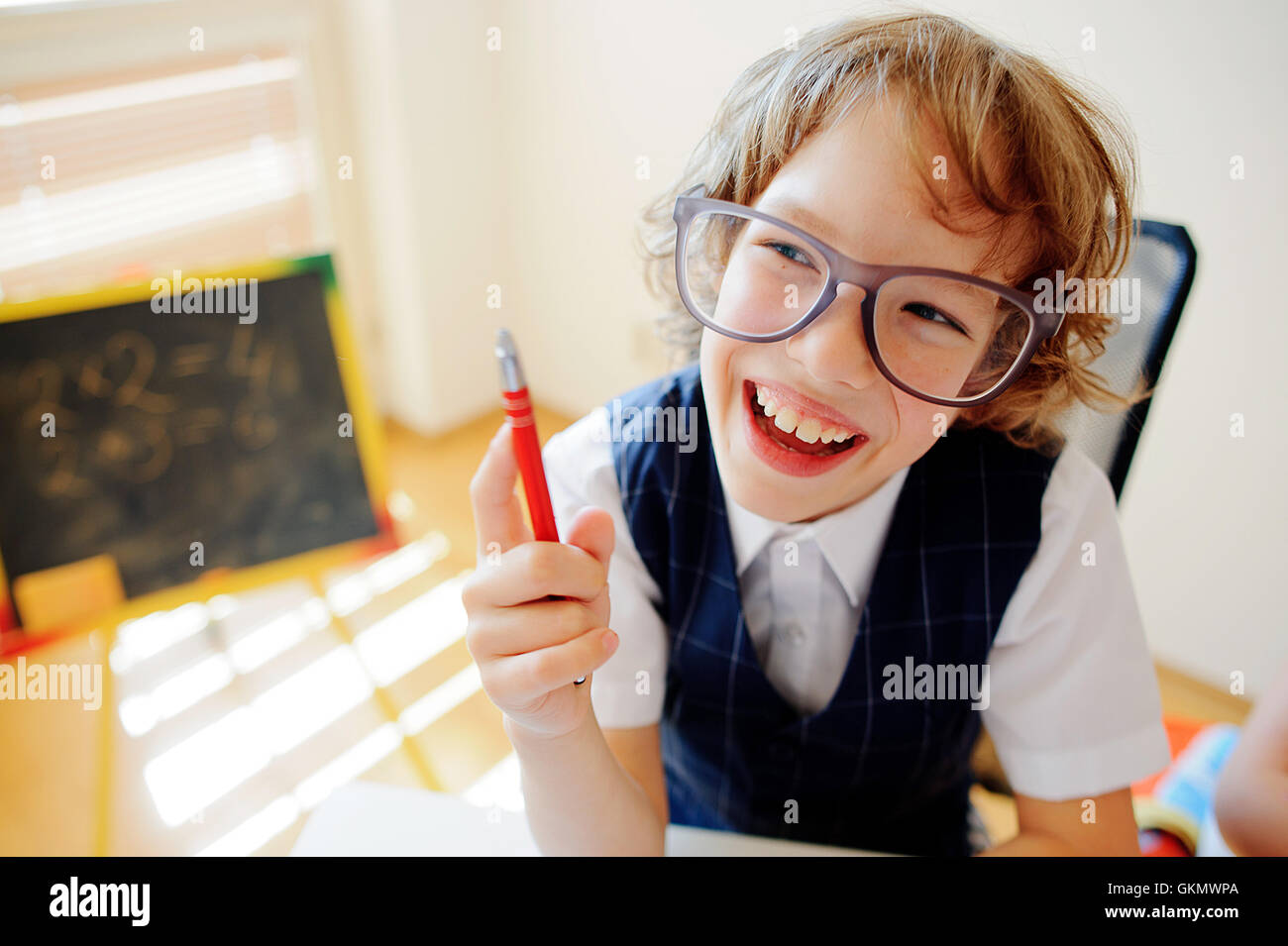 Funny little schoolboy in glasses sits at a school desk. It is a ...