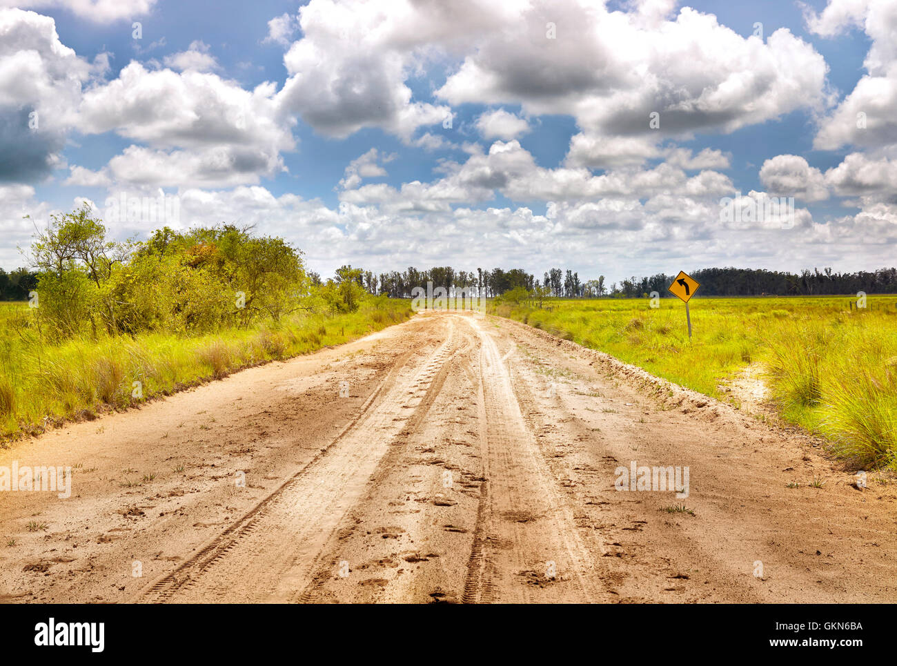 Turn left balck over yellow sign with soil sandy road in countryside. Cinematic road landcape. Argentina. South America Stock Photo