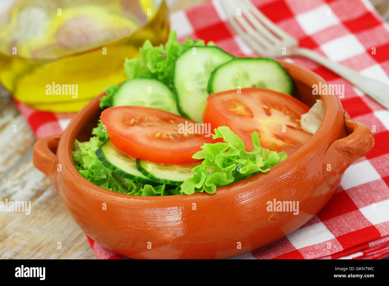 Fresh green salad consisting of lettuce, tomatoes and cucumbers in clay bowl on checkered cloth Stock Photo