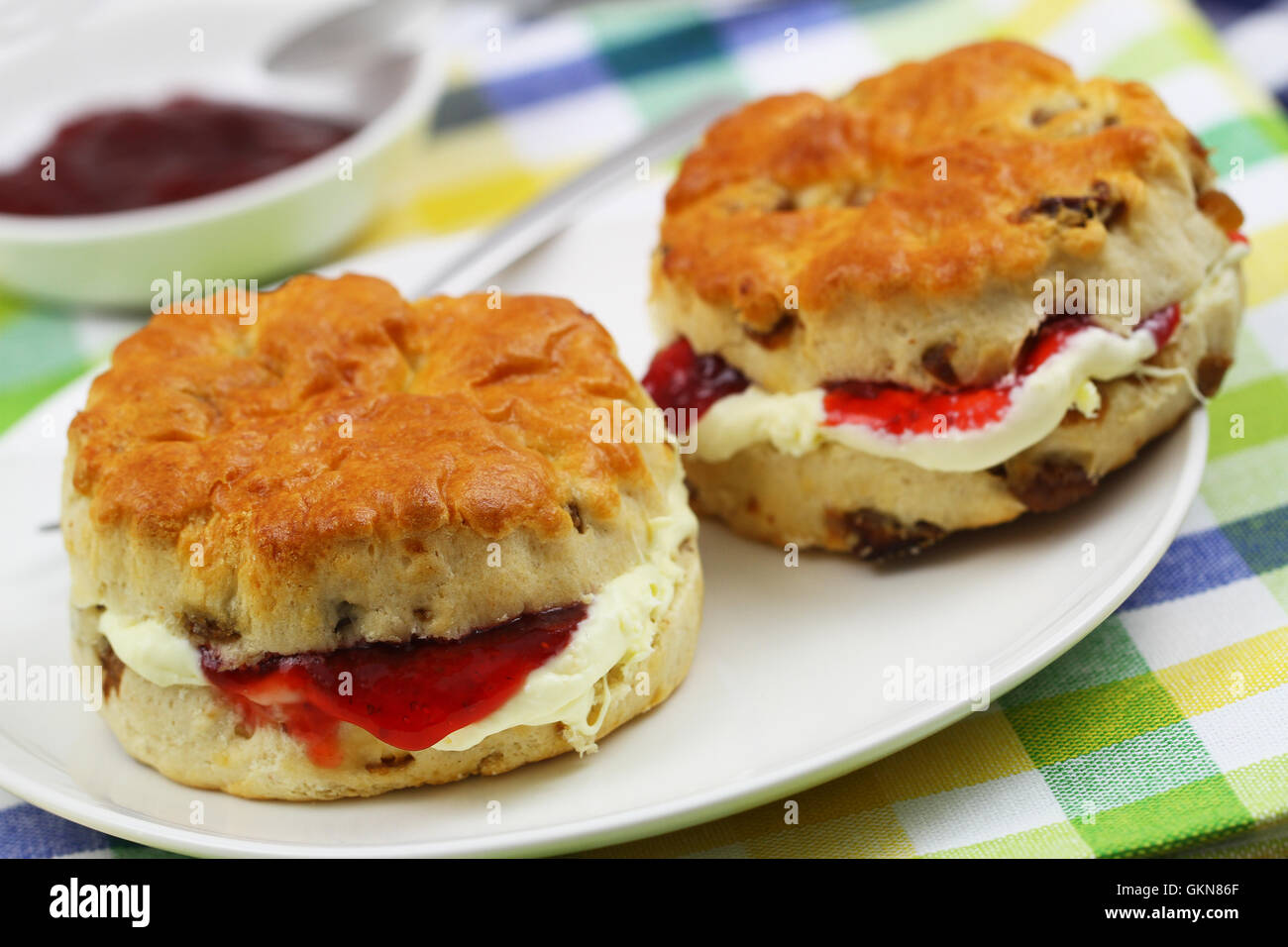 Freshly baked English scones with clotted cream and strawberry jam on checkered cloth Stock Photo