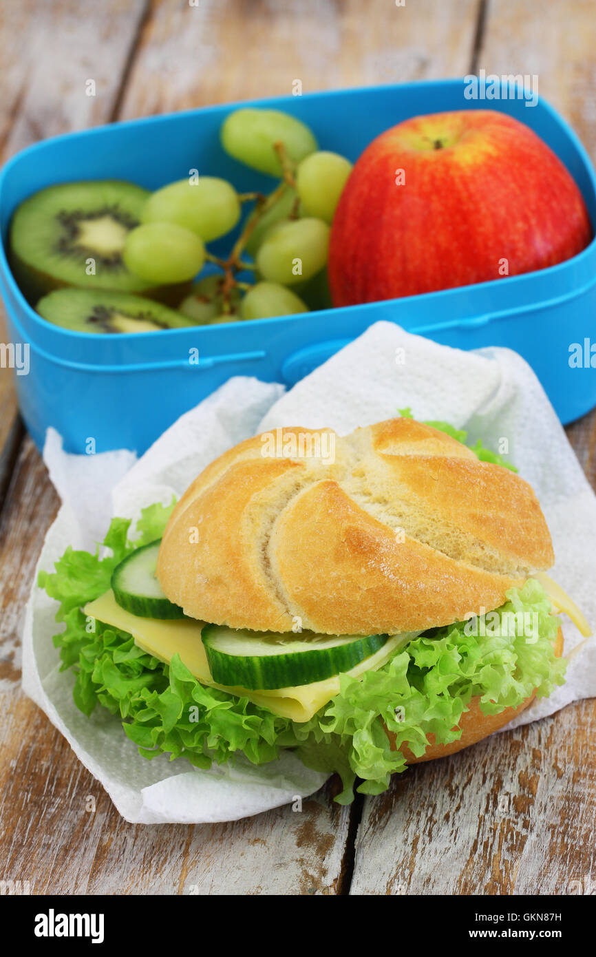 Cheese roll with lettuce and cucumber and lunch box with fresh fruit Stock Photo