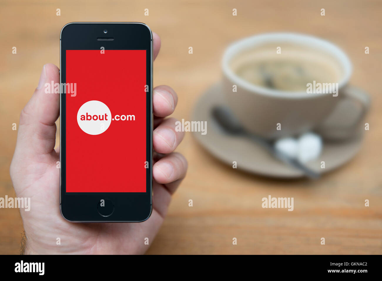 A man looks at his iPhone which displays the About.com logo, while sat with a cup of coffee (Editorial use only). Stock Photo