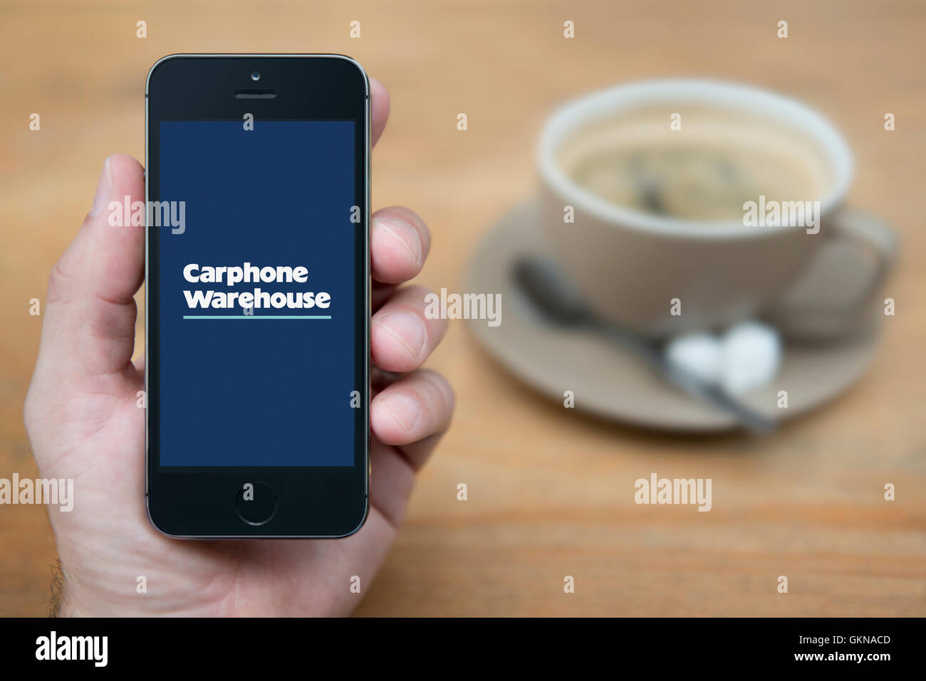 A man looks at his iPhone which displays the Carphone Warehouse logo, while sat with a cup of coffee (Editorial use only). Stock Photo