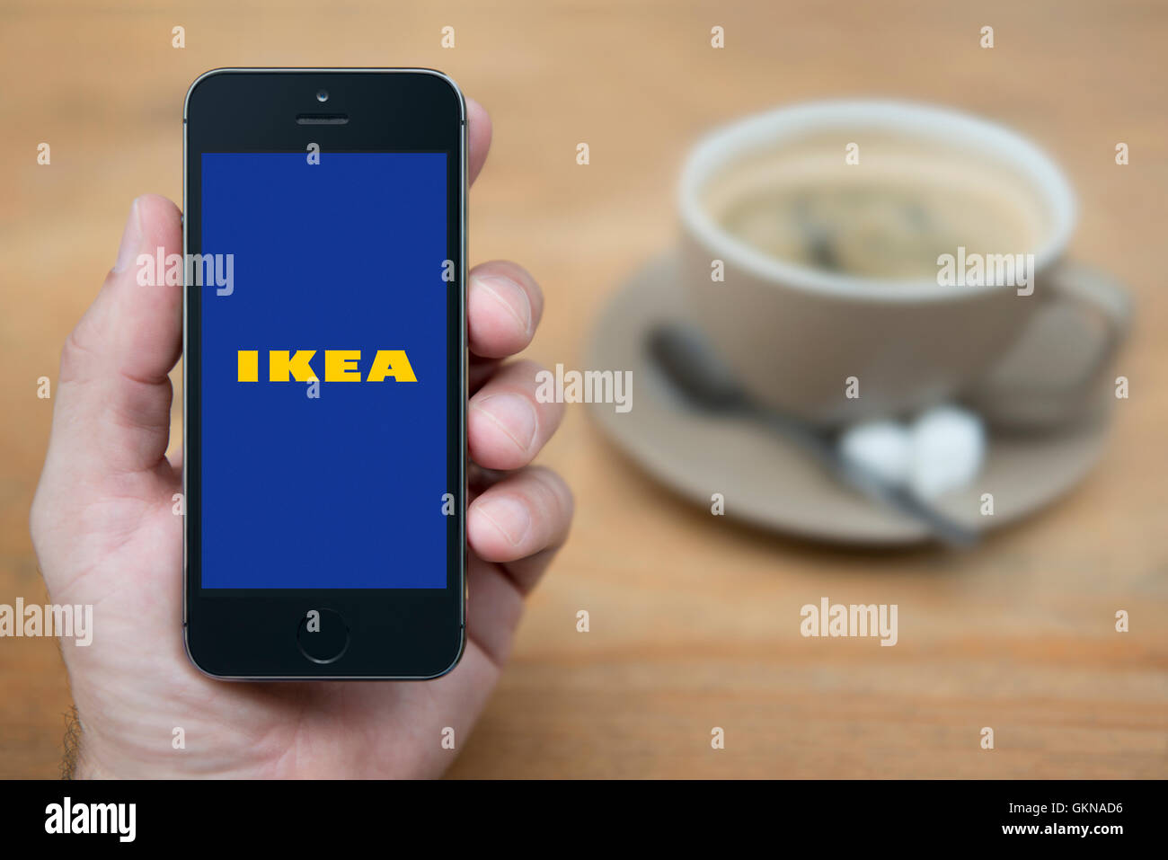 A man looks at his iPhone which displays the IKEA logo, while sat with a cup of coffee (Editorial use only). Stock Photo