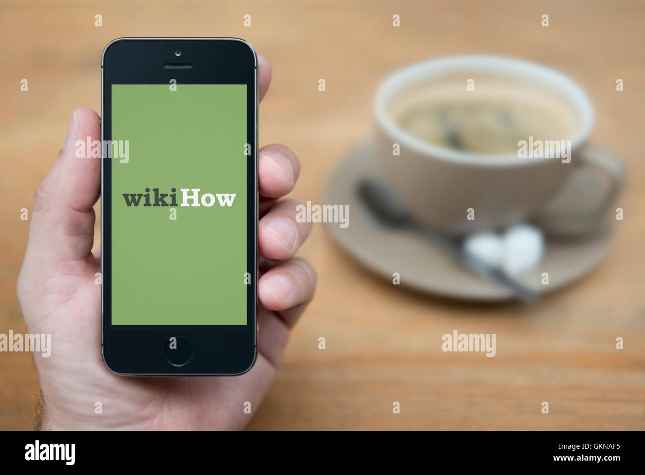 A man looks at his iPhone which displays the WikiHow logo, while sat with a cup of coffee (Editorial use only). Stock Photo