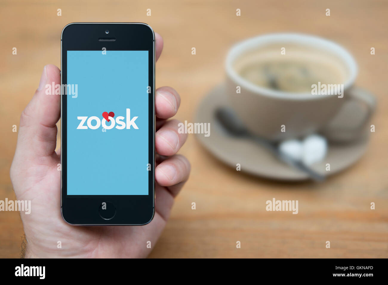 A man looks at his iPhone which displays the Zoosk logo, while sat with a cup of coffee (Editorial use only). Stock Photo