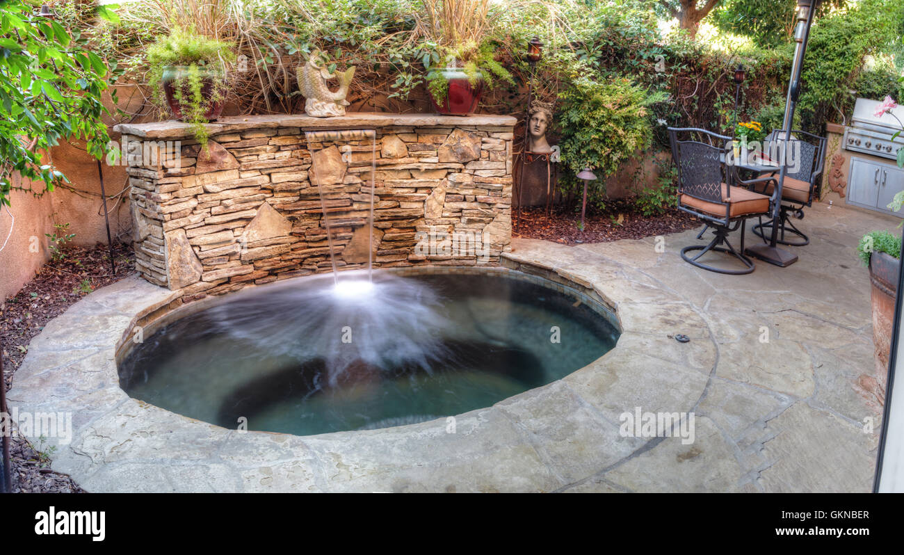 Irvine, CA, USA – August 19, 2016: Oval hot tub spa with waterfall and feng shui garden decor located in a private small patio w Stock Photo