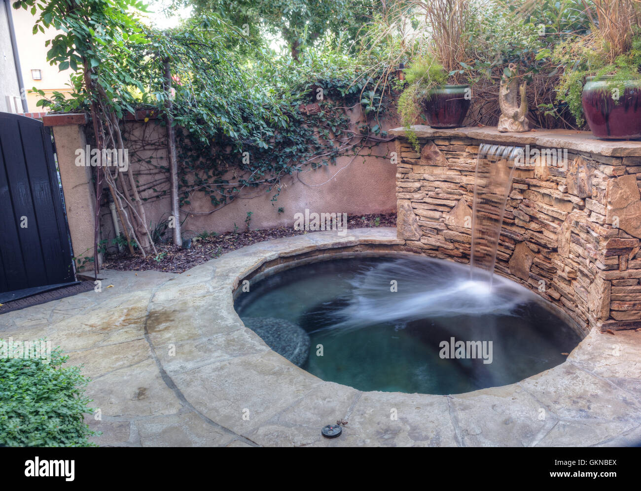 Irvine, CA, USA – August 19, 2016: Oval hot tub spa with waterfall and feng shui garden decor located in a private small patio w Stock Photo