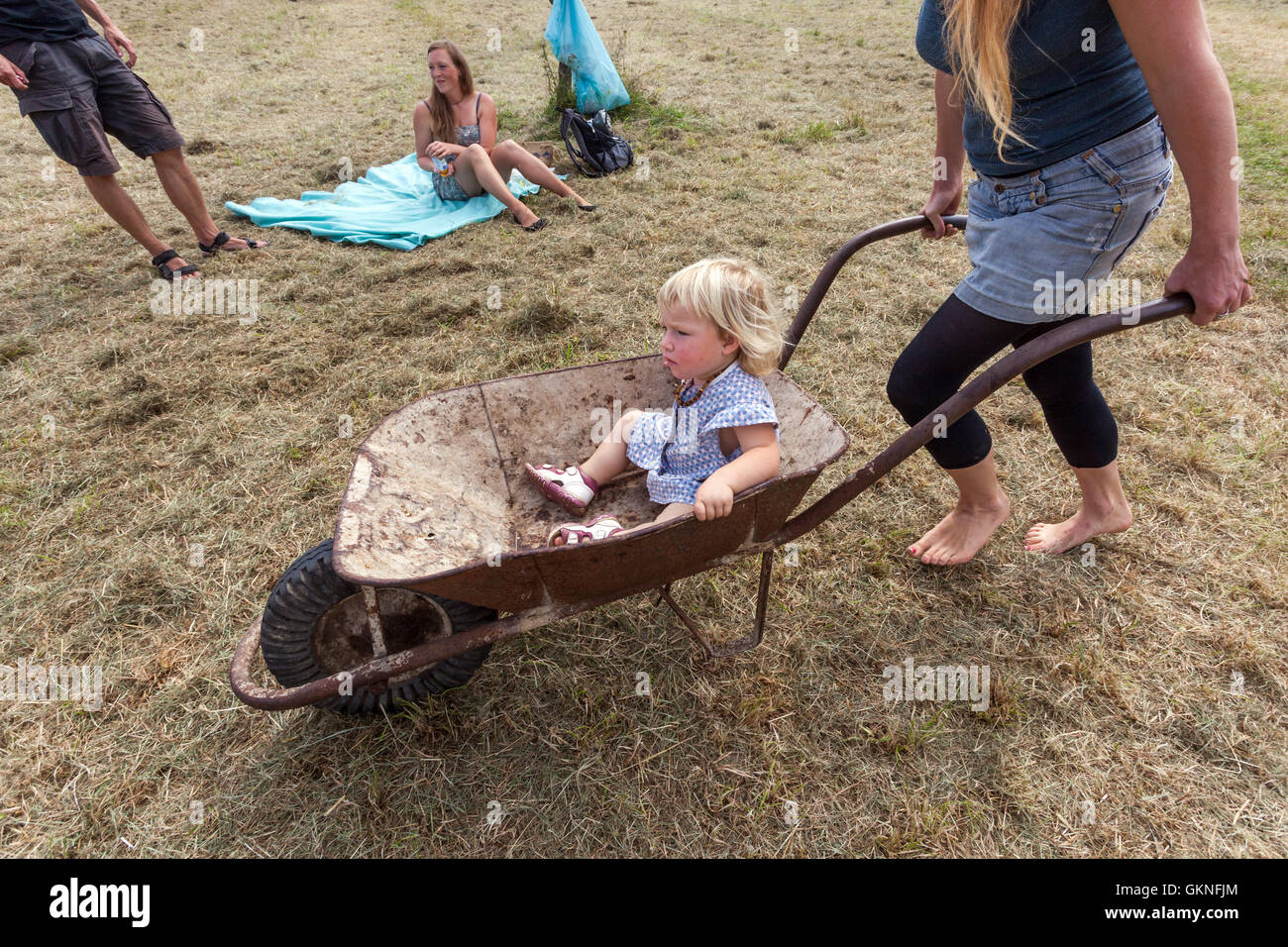 Woman pushing a wheelbarrow with a toddler in summer Stock Photo