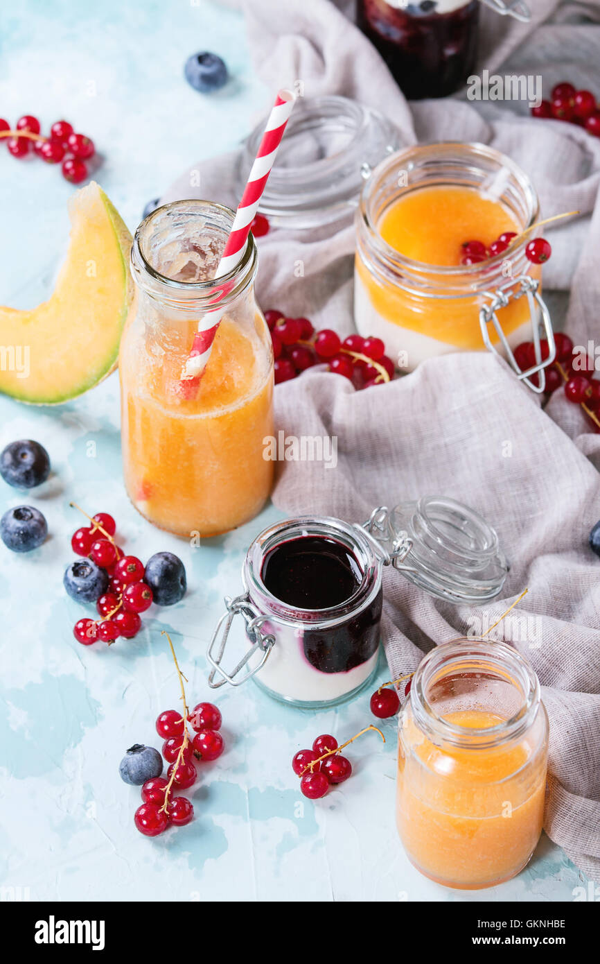 Variety of melon and blueberries smoothie in glass jars and bottle with yogurt and red currant berry, served on light blue textu Stock Photo