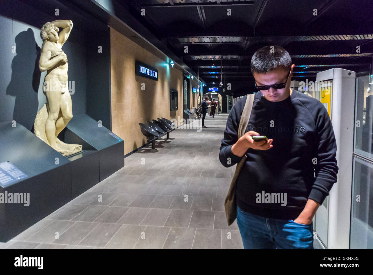 Paris, France, Metro, Underground, Subway Station, Chinese Man Looking at Smart Phone, at Louvre Rivoli Station, with Art Work on DIsplay on Quay, Platform public Stock Photo