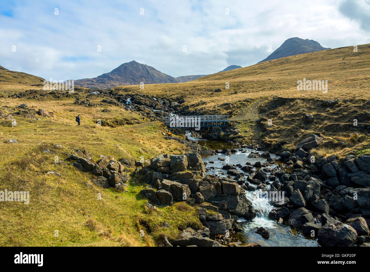 A walker at the bridge over the Abhainn Rangail burn, with the peaks of Barkeval and Trollaval behind, Isle of Rum, Scotland, UK Stock Photo