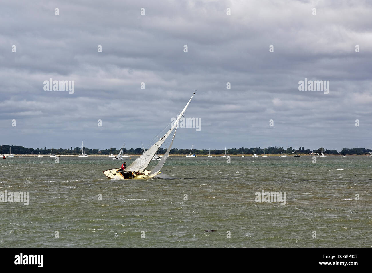 A sailing boat heels over, decks awash and running fast driven by strong winds. Stock Photo
