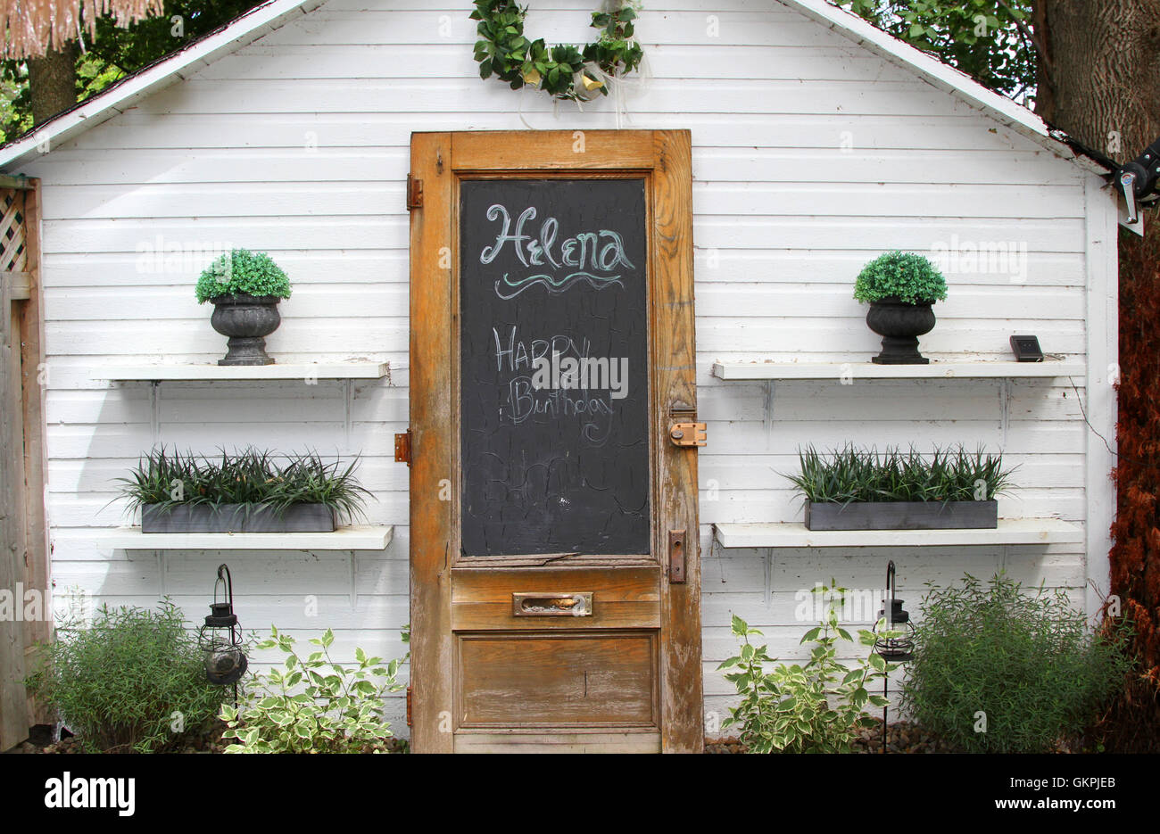 White shed with plants on shelves and door with a chalkboard Stock Photo