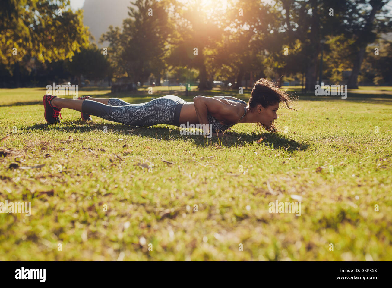 Horizontal shot of a sporty and fit young woman in sportswear working out outdoors on summer day. Sportswoman doing push ups exe Stock Photo