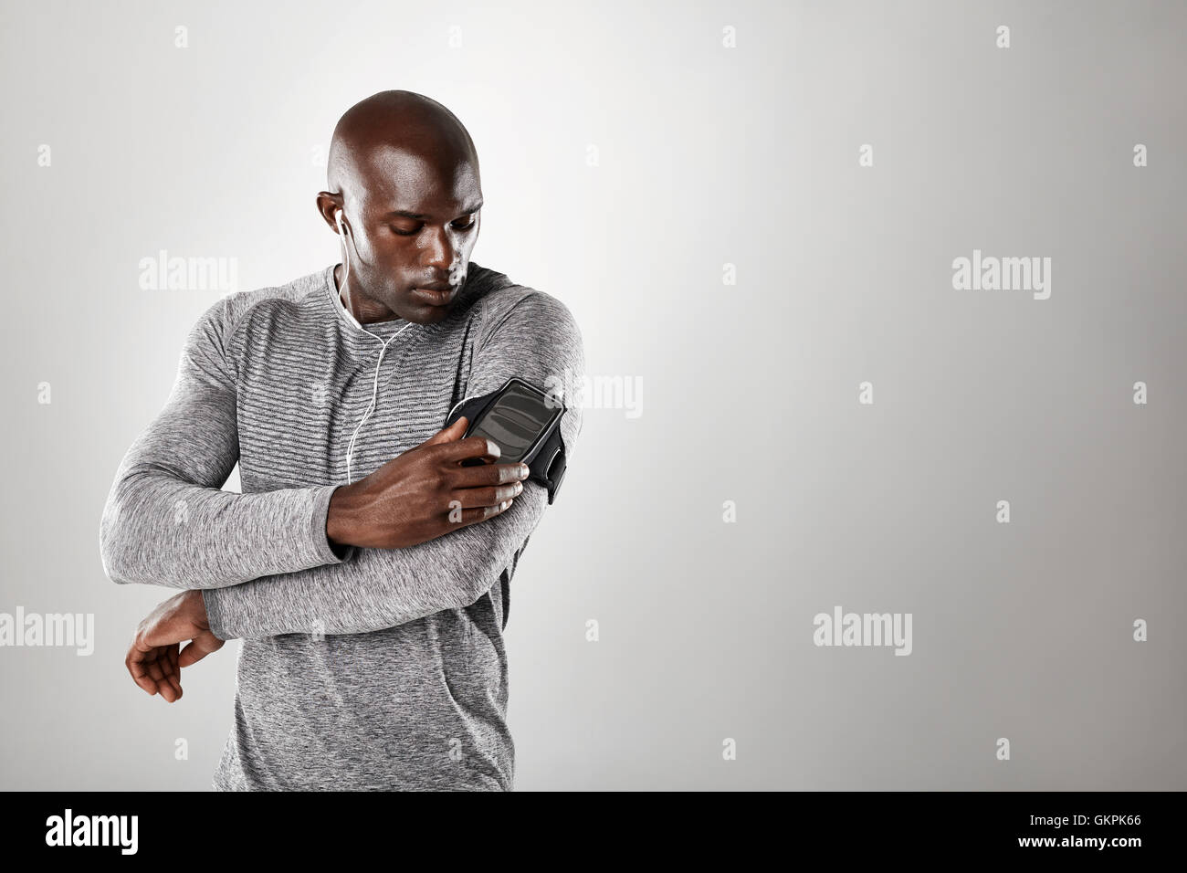 Studio shot of african muscular man listening to music on mobile phone. Fit young man against grey background with copy space. Stock Photo