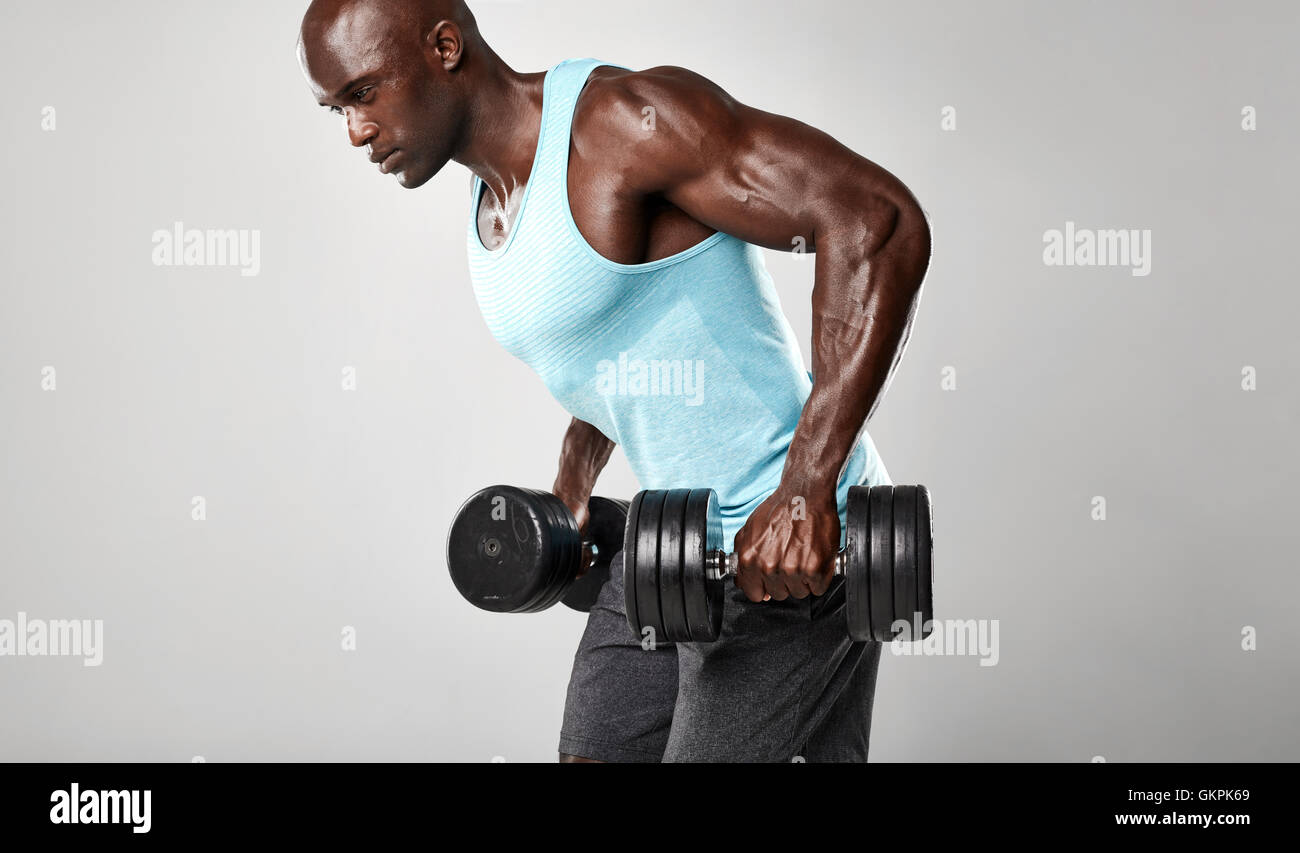 Healthy young african man exercising with dumbbells. Muscular black male model lifting heavy dumbbells against grey background. Stock Photo