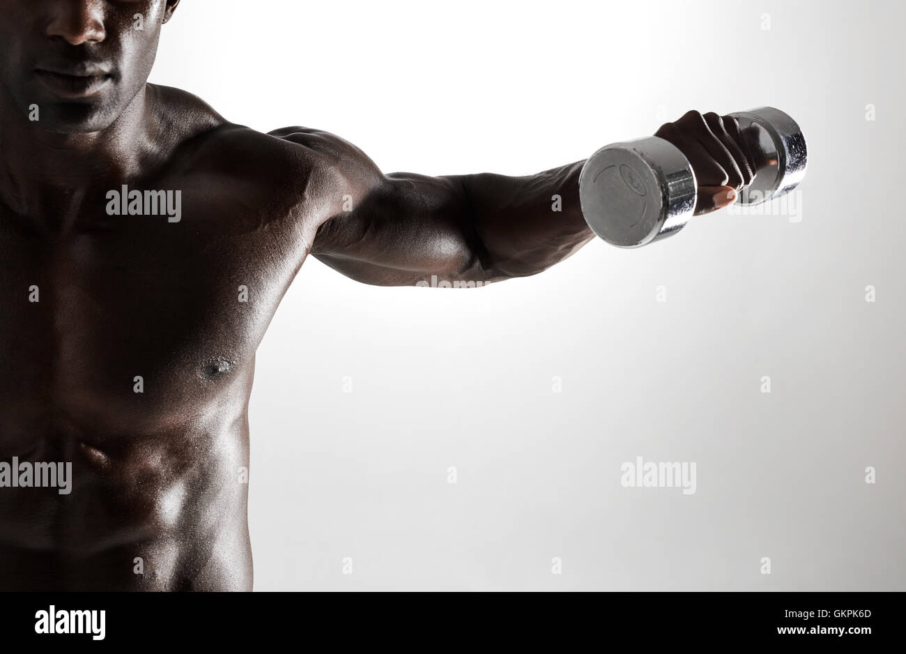 Shot of young muscular man doing dumbbell exercise for arms. African fitness model working out with dumbbells on grey background Stock Photo