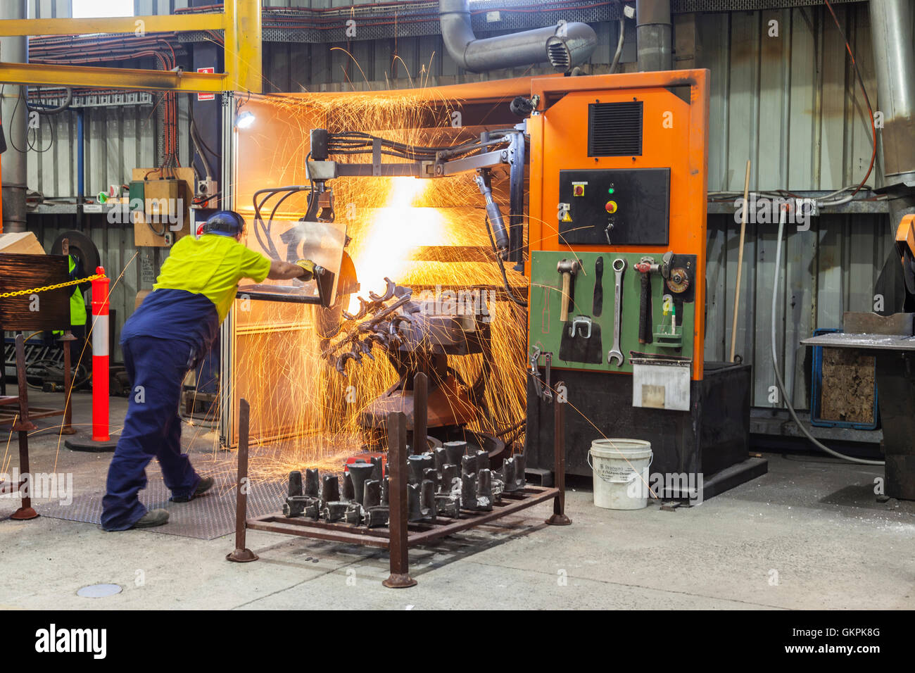 workman grinding and cutting away cast metal components from its